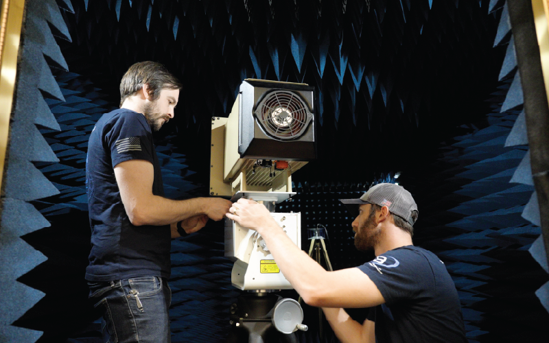 Two men work on device inside anechoic chamber