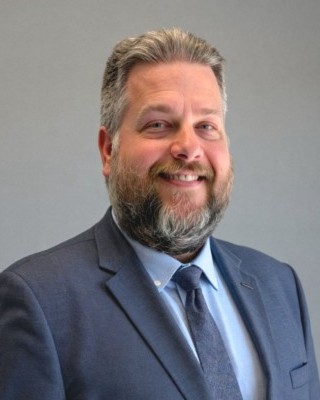 Headshot of Barry Polakowski, a man smiling wearing a blue suit and tie