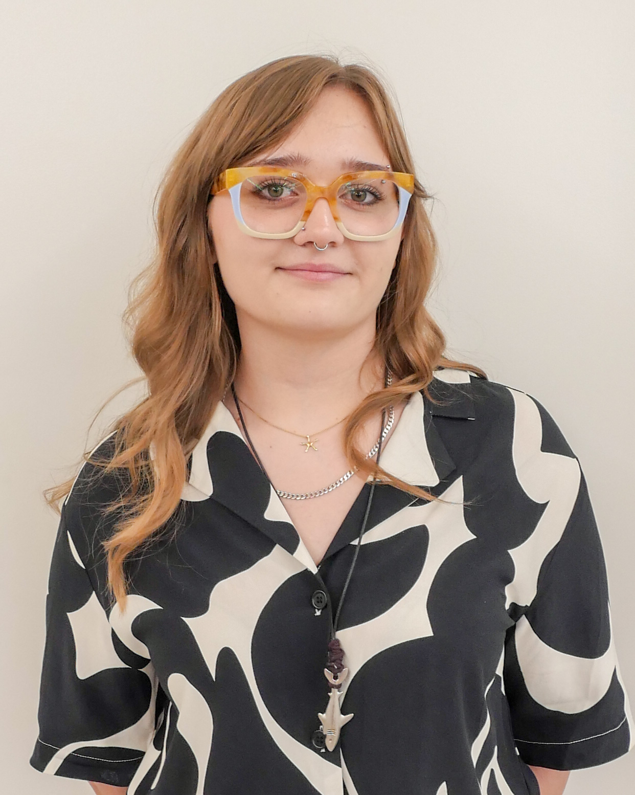 Headshot of Charlotte El-Khodary, smiling and wearing colorful glasses and a black and white patterned shirt