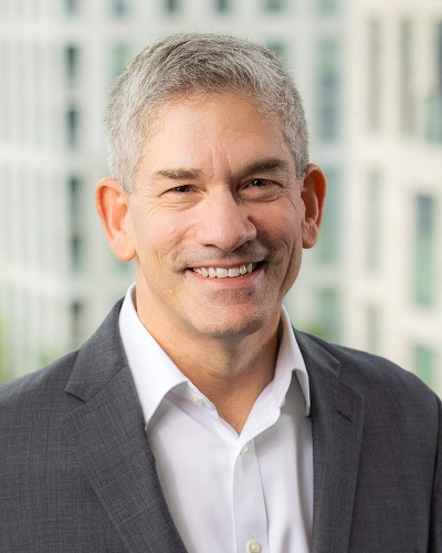 Headshot of Garry Schwartz, a man smiling wearing a white collared shirt and gray suit jacket