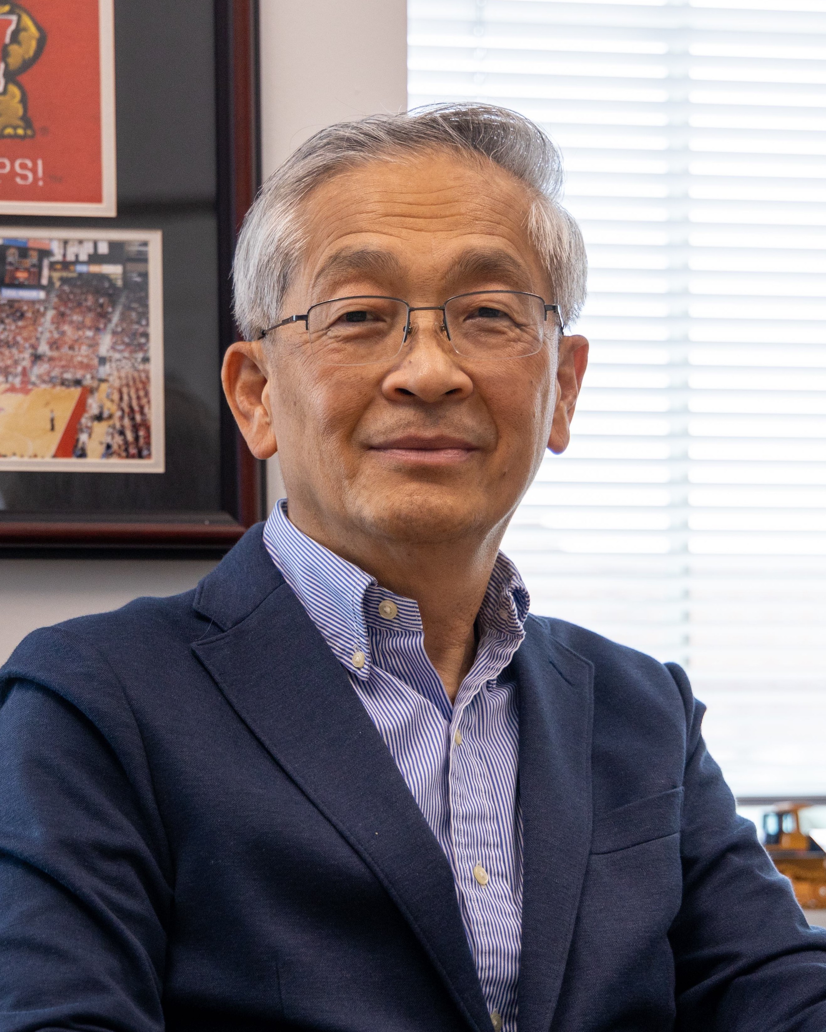 Headshot of Jay Lee, a man smiling wearing glasses, a dark suit, and a blue shirt