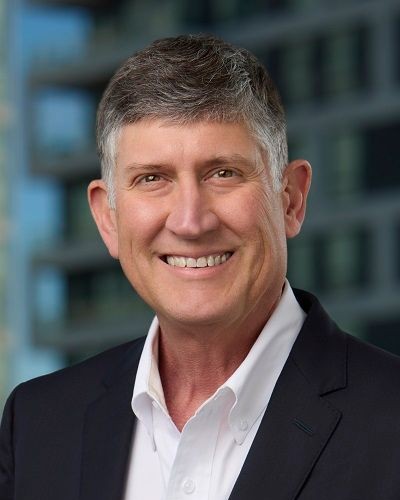 Headshot of John Bell, a man smiling wearing a dark jacket and white shirt