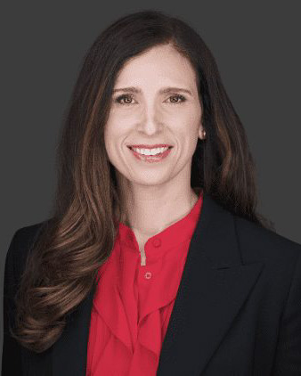 Headshot of Katie Selbe, a woman smiling and wearing a red button down shirt and black suit jacket