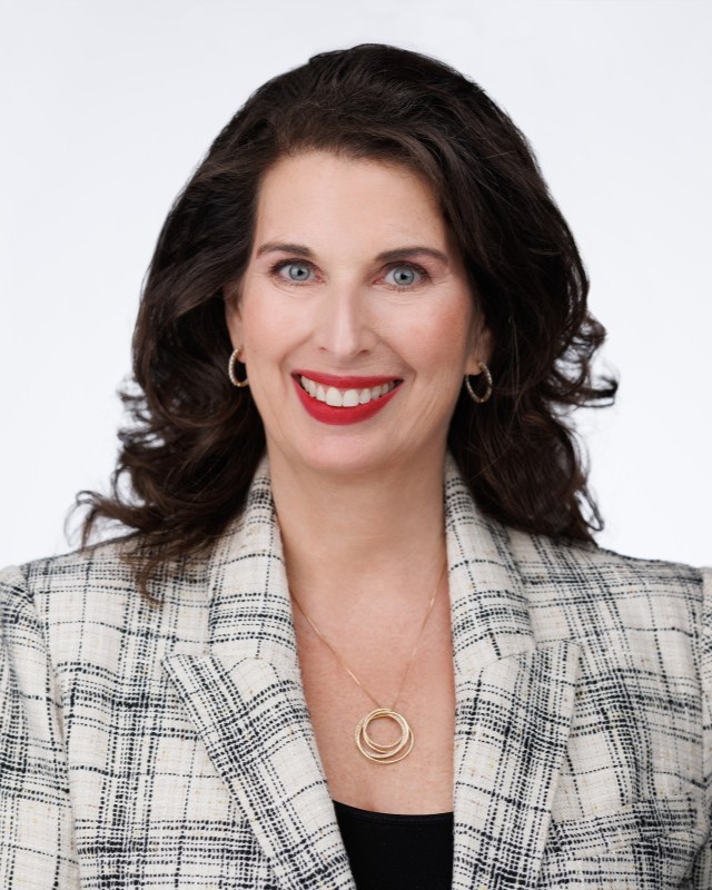 Headshot of Nicole Goldman, a woman smiling wearing a patterned jacket and black shirt