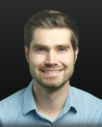 Headshot of Philip Luca, a man smiling and wearing a blue and white striped collared shirt
