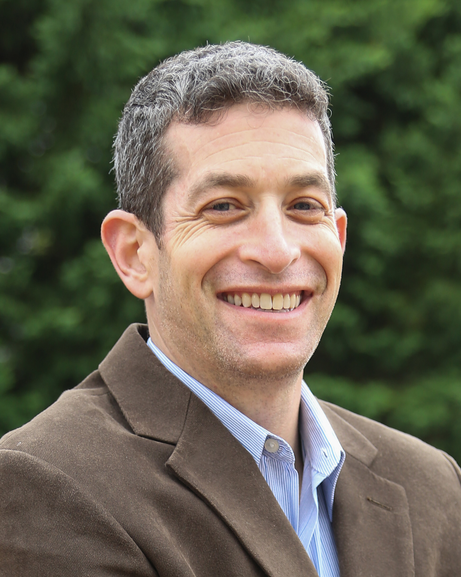 Headshot of Brian Weiss who is smiling and wearing a gray jacket and blue button down shirt