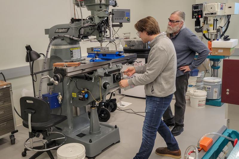 Instructor watches student use milling machine