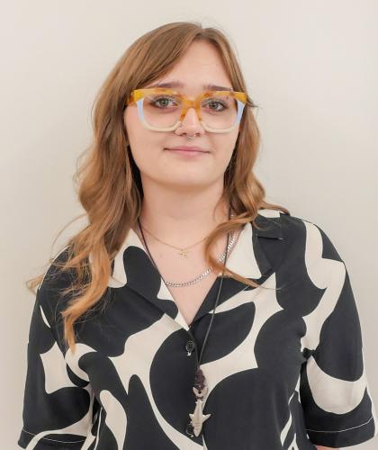 Headshot of Charlotte El-Khodary, smiling and wearing colorful glasses and a black and white patterned shirt