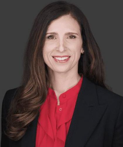 Headshot of Katie Selbe, a woman smiling and wearing a red button down shirt and black suit jacket